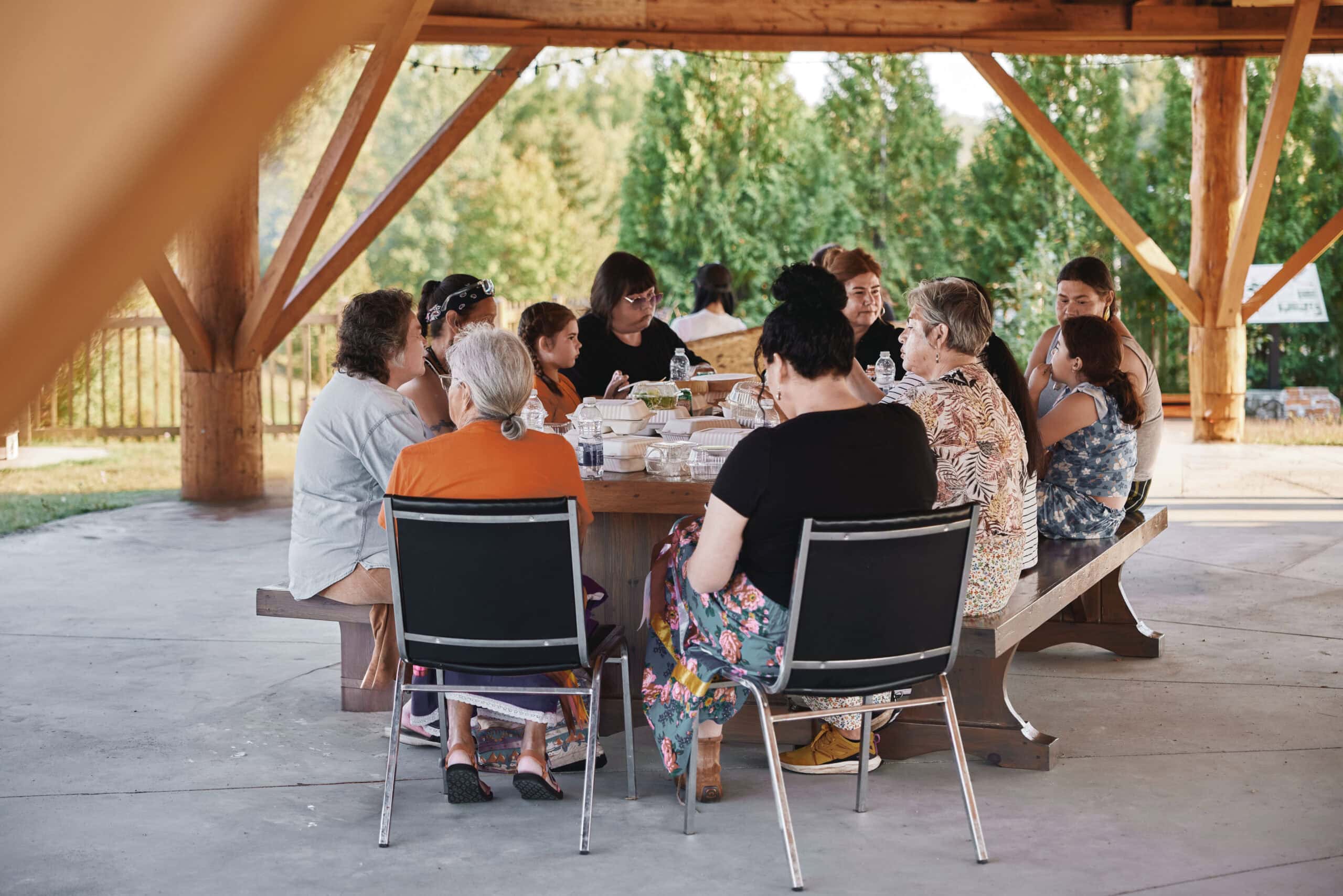 A group of Anicinabe women and girls eat at a picnic table under the arbour in Kebaowek.